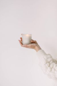 Woman's arms and hands in white sweater holding a white candle
