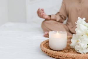 Woman sat on bed meditating with a lit white candle