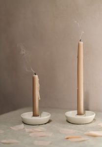 Two beige candlesticks with white holders with smoke after being blown out