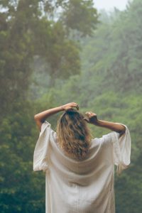 Woman's back wearing a white dress and facing a green rainforest
