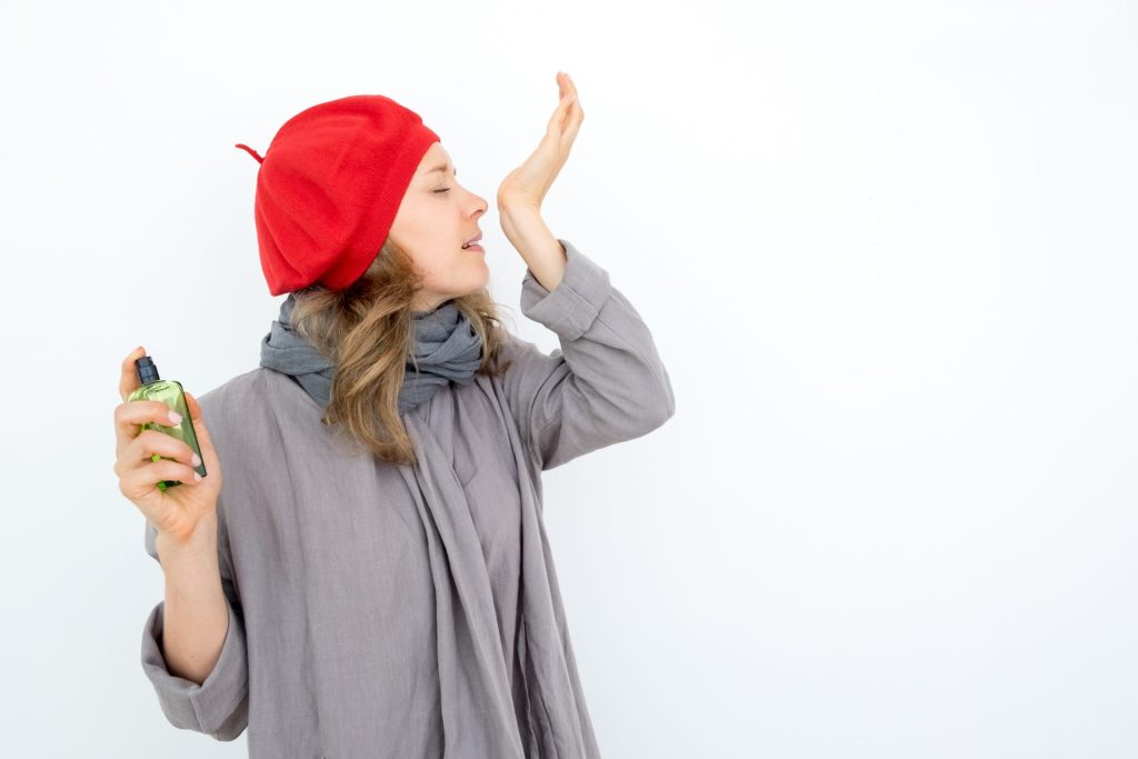 Woman wearing red beret smelling perfume on wrist